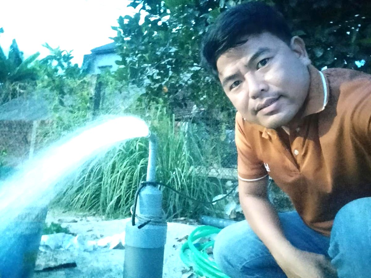 Pastor Quang kneeling beside the new well as clean water pours out