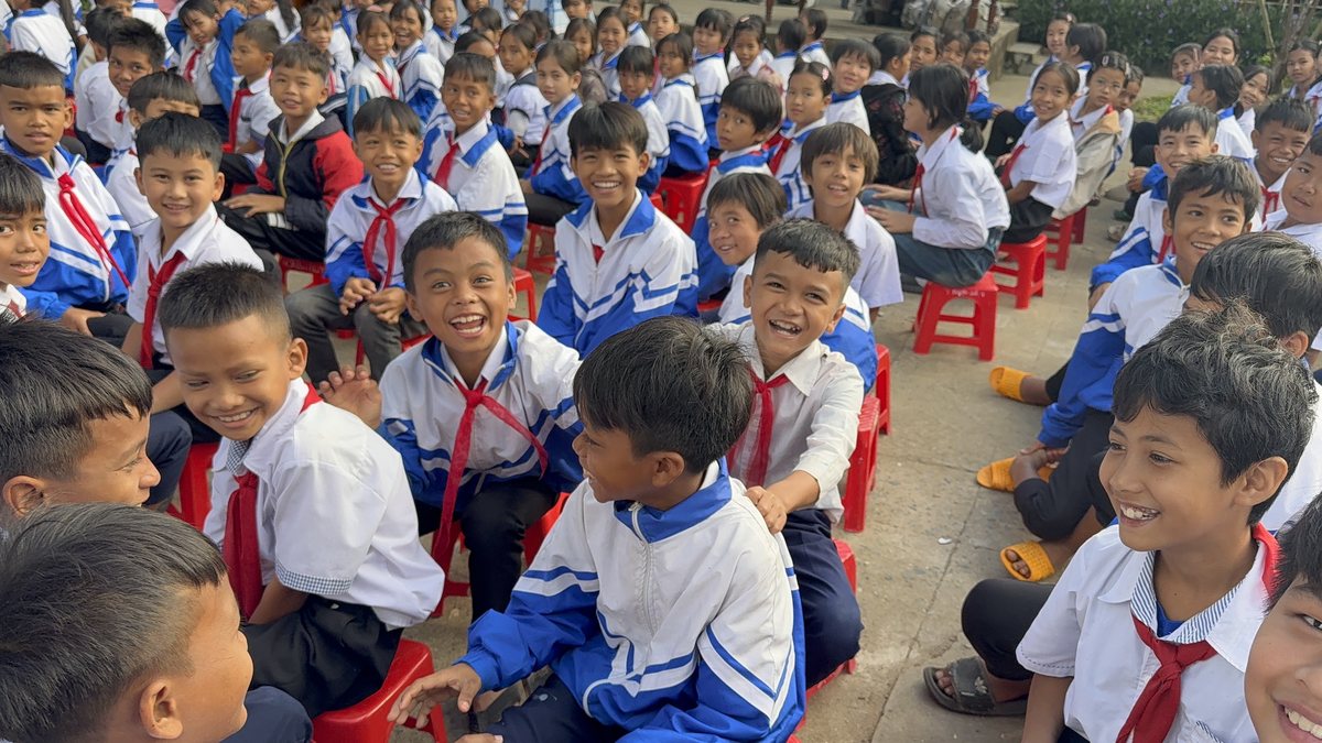 Smiling school children in blue and white uniforms seated outdoors in the Highlands