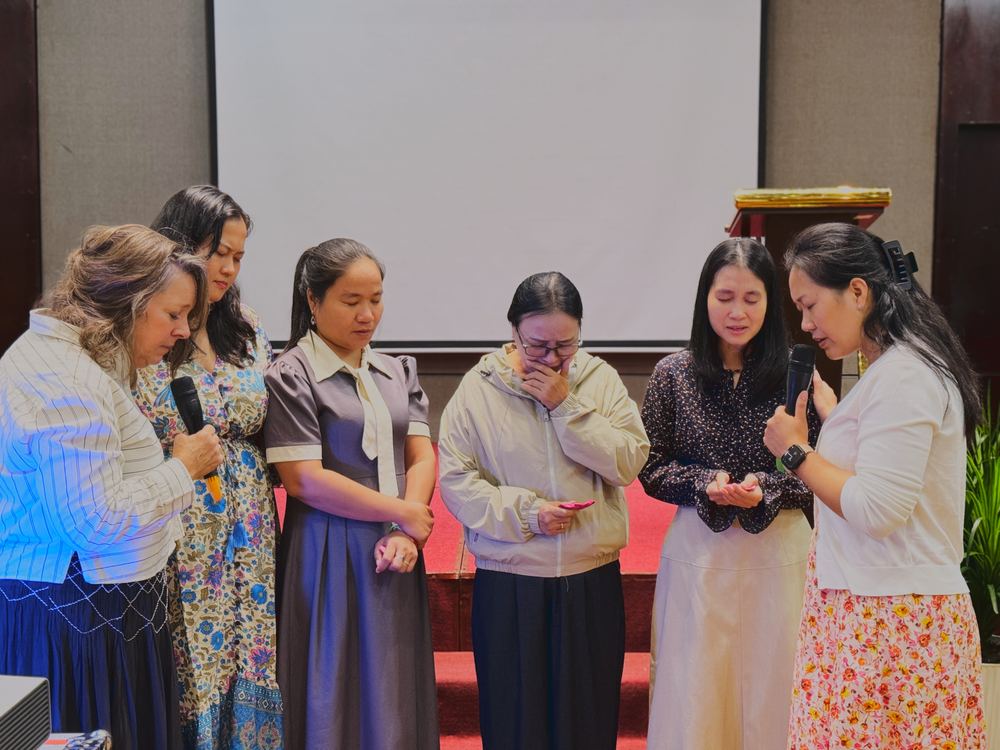 Women praying together at the front of the conference hall