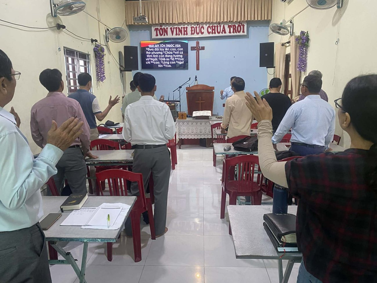 Pastors standing in worship at their desks during a training week, Bibles and notebooks open